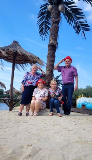 grupa mieszkańców pozuje do zdjęcia na plaży pod palmą