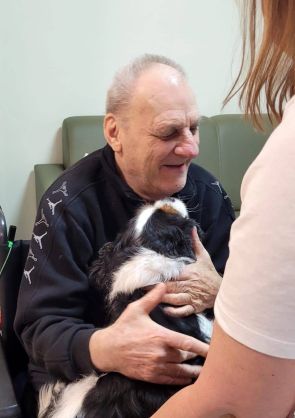 uśmiechnięty mieszkaniec obejmuje czarnobiałego średnich rozmiarów psa podczas dogoterapii