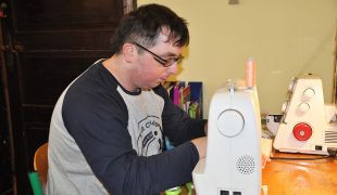 Uczestnik zajęć w pracowni krawiectwa szyjący na maszynie do szycia