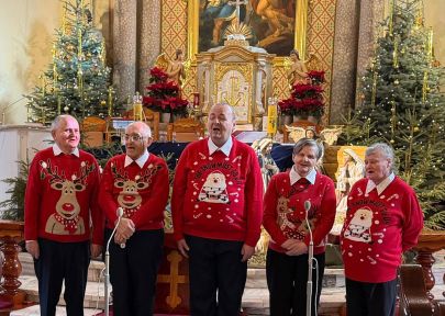 pięcioro mieszkańców ubranych w bożonarodzeniowe swetry śpiewa w kościele, w tle ołtarz