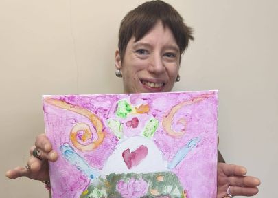 zadowolona mieszkanka trzymając w rękach prezentuje swoją prace plastyczną - kolorowy obraz 